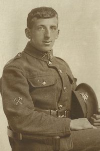 A British Army soldier seated in a photographic studio. He is in uniform and facing the camera.