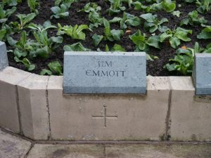 A greenish coloured stone on top of a memorial wall. It has the name Jim Emmott inscribed into the front face.