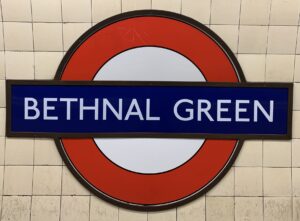 Bethnal Green London Undergraouns sign. a Red cirlse with a white centre and a dark blue horizontal band across the centre with the words BETHNAL GREEN in white letters.
