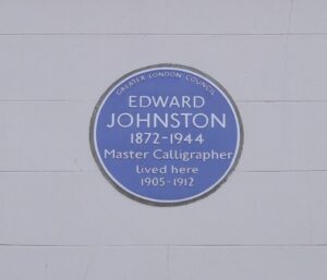 A blue plaque on a white wall. The words say: Edward Johnston 1872 - 1944 Master Calligrapher Lived here 1905 - 1912.